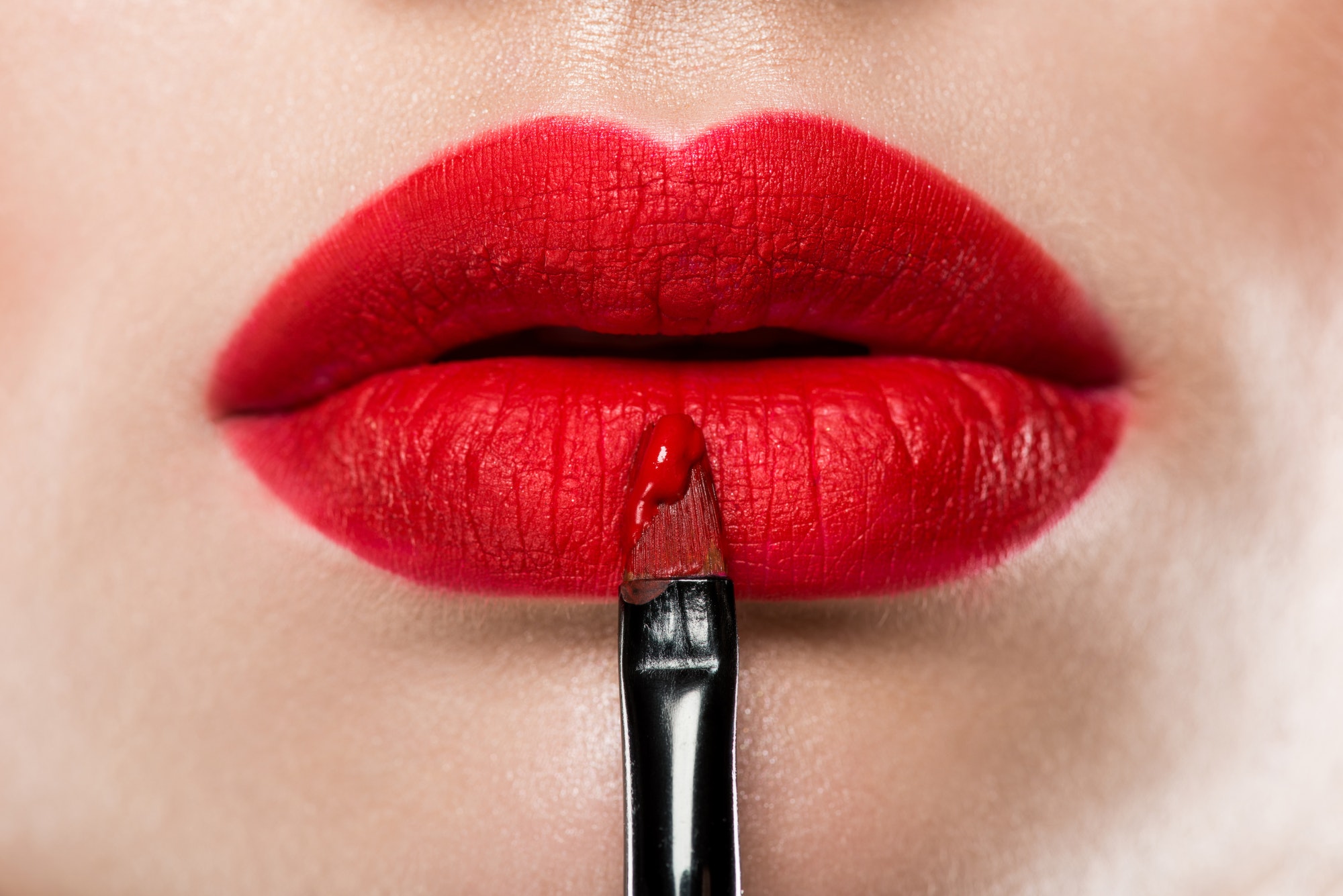 close up view of elegant woman applying red lipstick with cosmetic brush