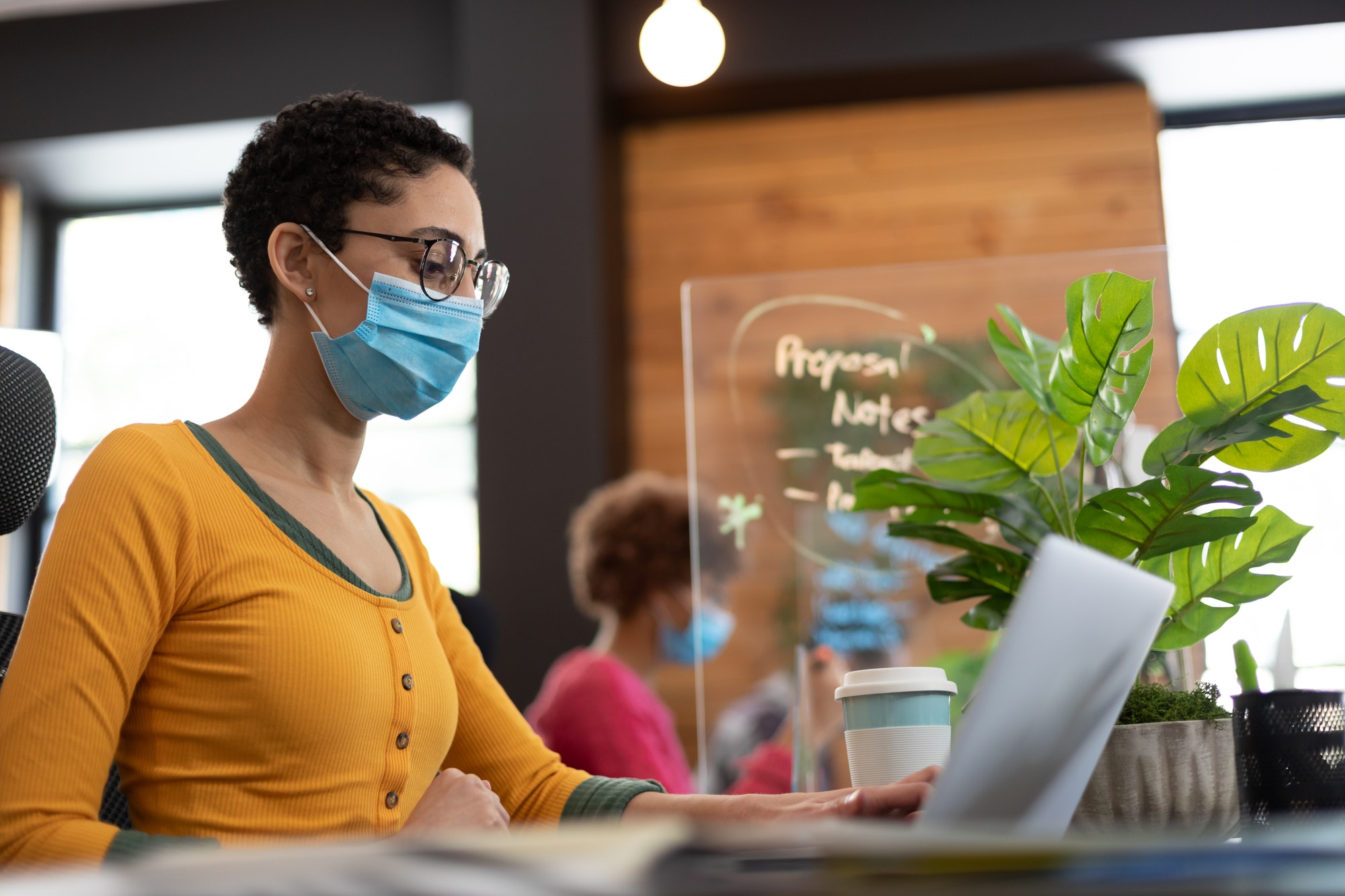 Mixed race woman wearing face mask working at desk in office